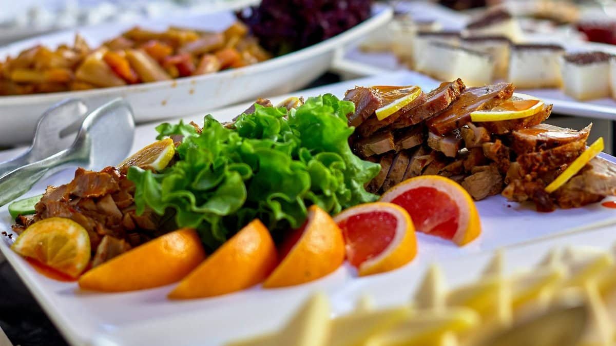 A vibrant buffet spread featuring sliced meats, fresh greens, and juicy citrus fruits on a serving board.