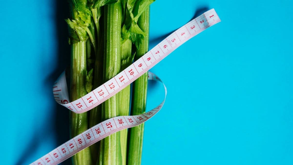 Close-up of celery stalks wrapped with measuring tape on a vibrant blue background, symbolizing health and diet.