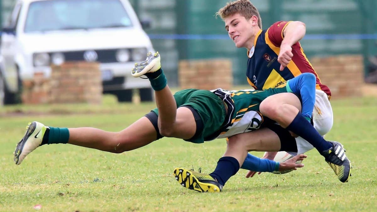 Two young athletes engaged in a dynamic rugby tackle during a competitive match.