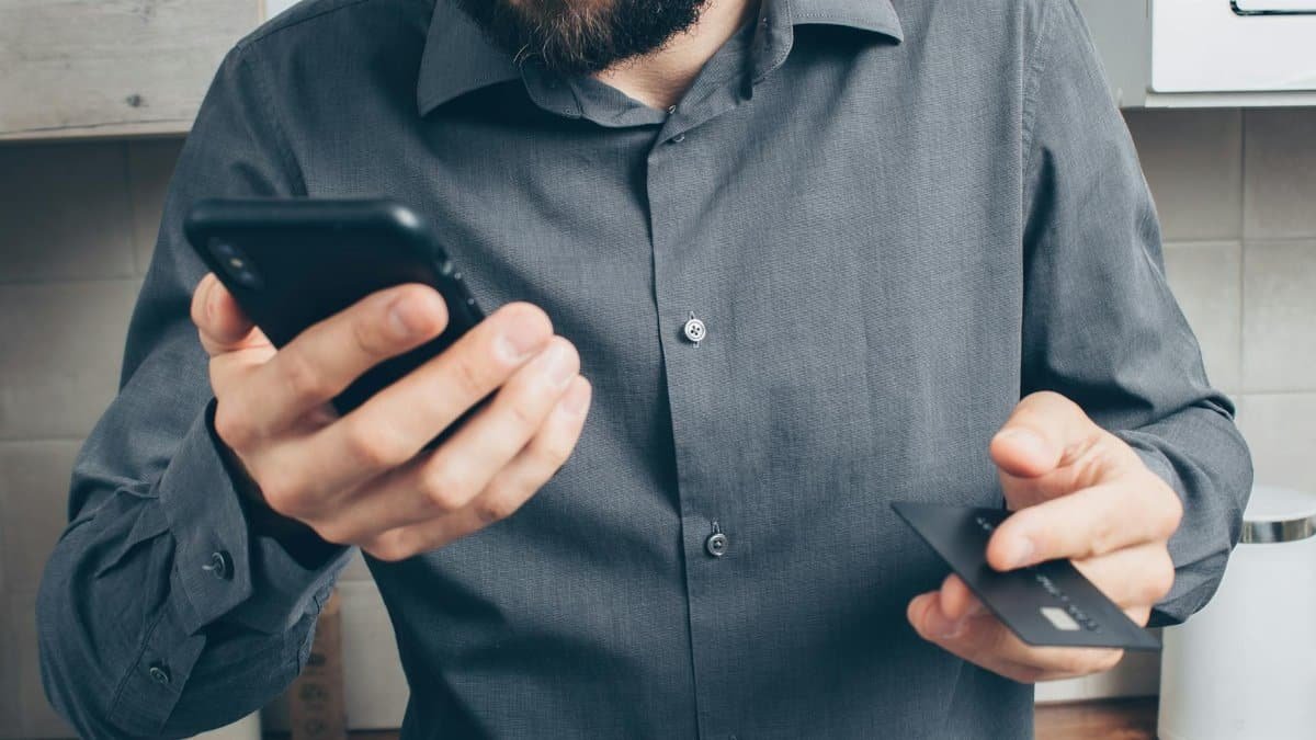 Close-up of a man using a smartphone for online payment with a credit card indoors.