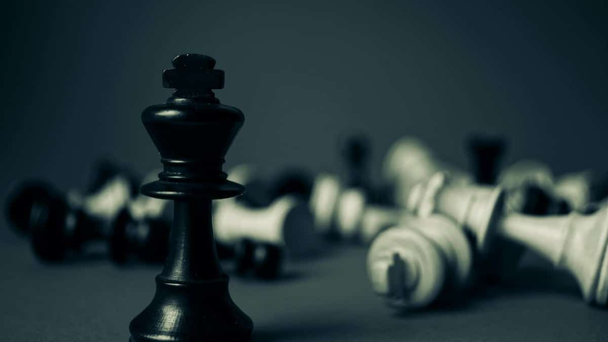 Black king chess piece stands tall among fallen pieces, symbolizing strategy and triumph.