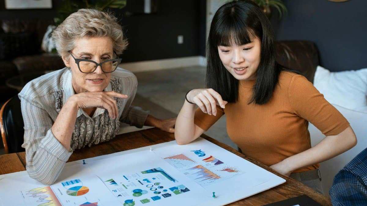 Two women discussing charts at a modern office desk, showcasing business collaboration.