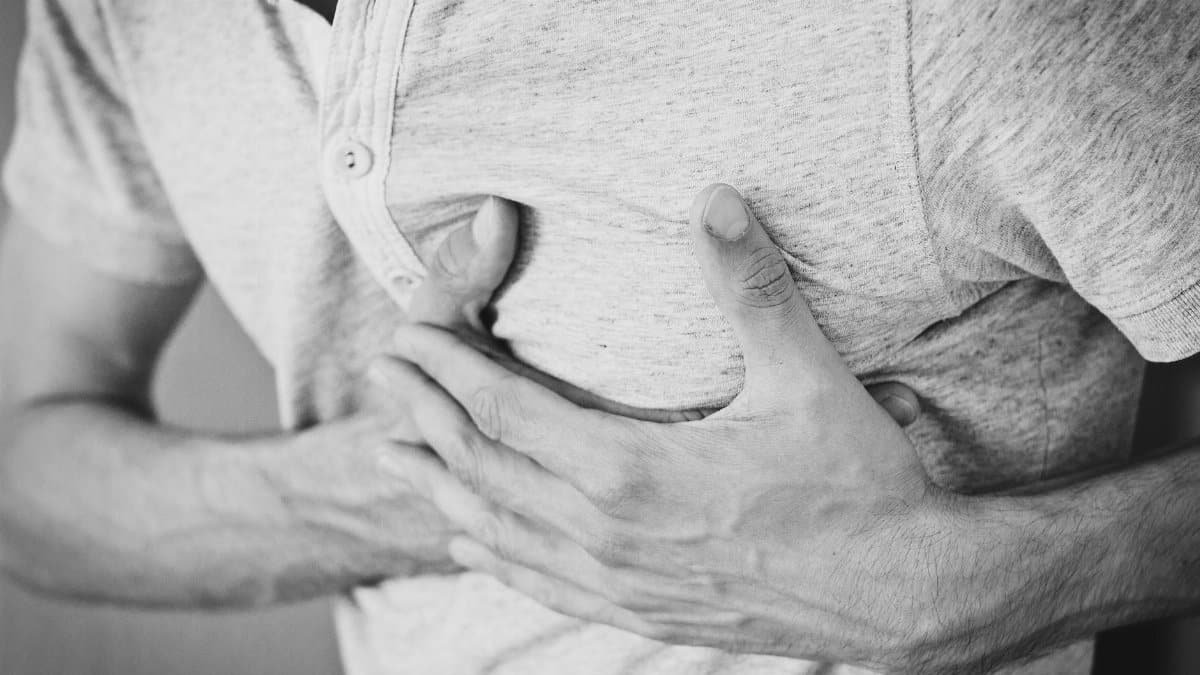 Black and white photo of a man clutching his chest, indicating discomfort or pain.