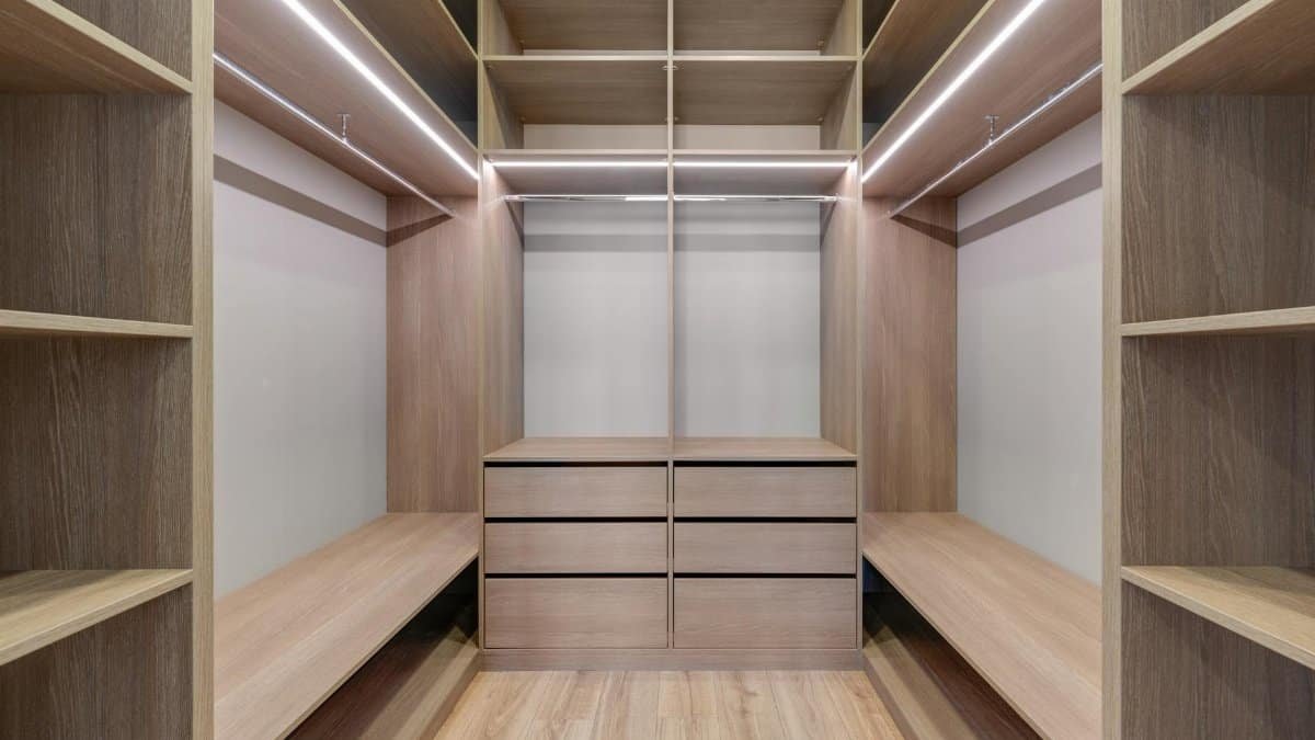 Spacious walk-in closet with wooden shelves and LED lighting creates a minimalist and modern design.