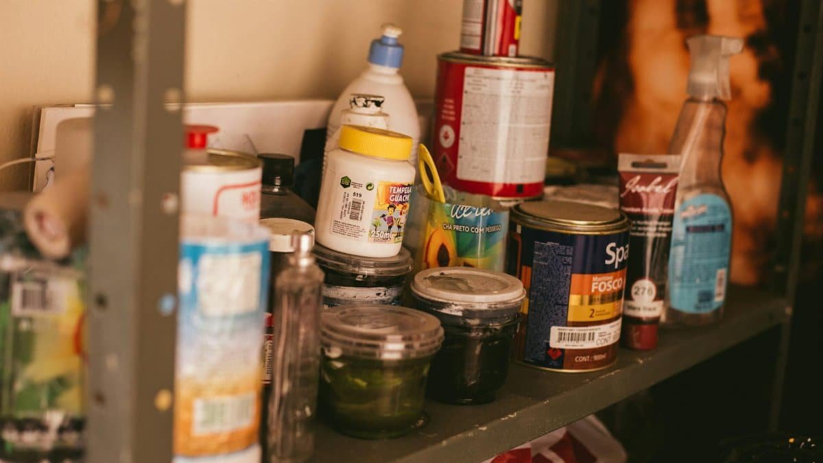 A cluttered shelf in a workshop stocked with various paint containers and supplies.