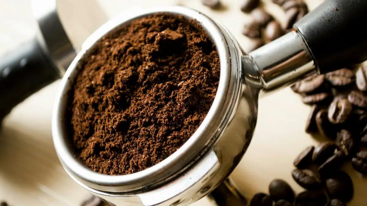 Close-up of freshly ground coffee in a portafilter with scattered coffee beans.