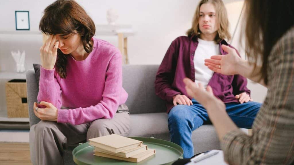 A couple undergoing therapy, expressing emotions on a sofa in a counseling office.