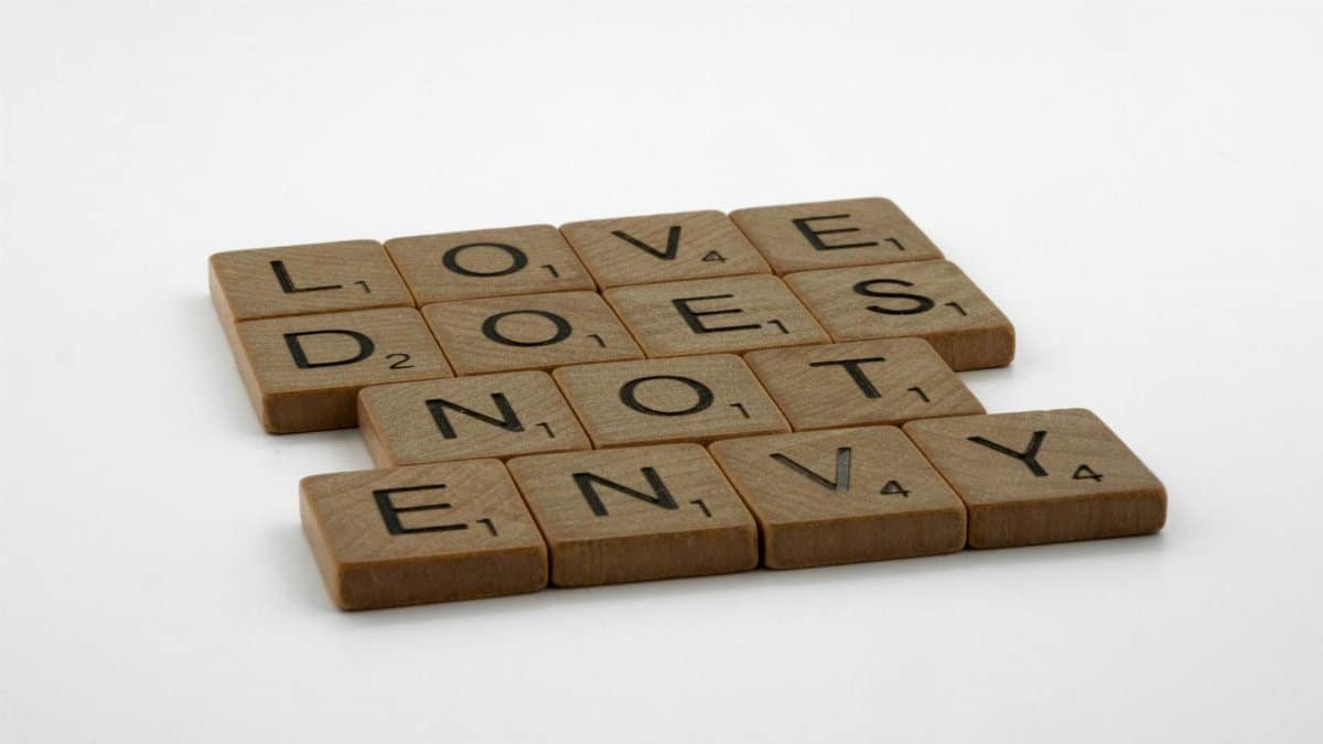 Inspirational quote 'Love Does Not Envy' spelled with Scrabble tiles on white background.