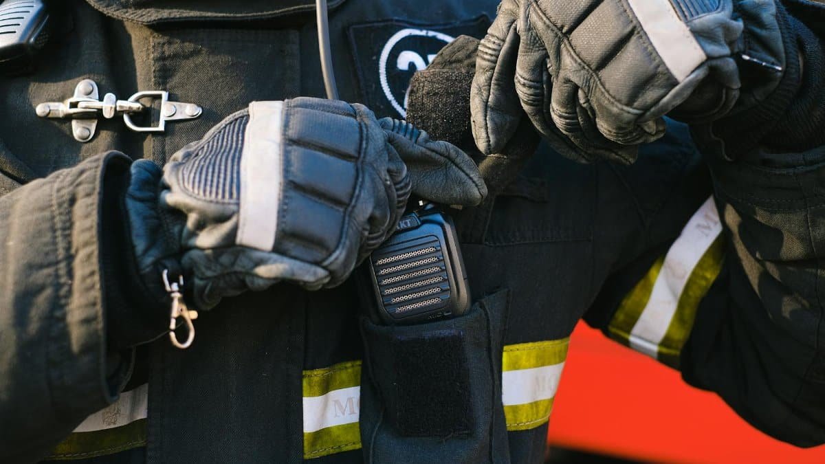 Close-up of a firefighter using a transceiver with gloved hands for communication.