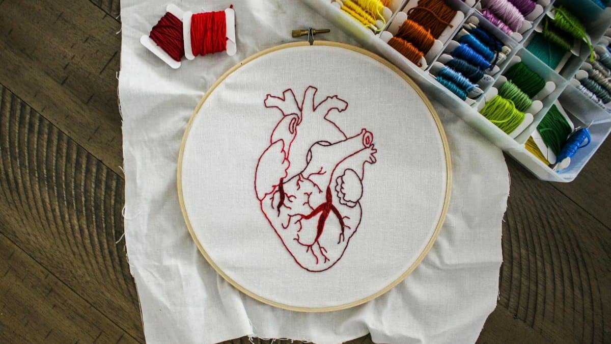 Close-up of an anatomical heart embroidery with vibrant threads on a wooden table.