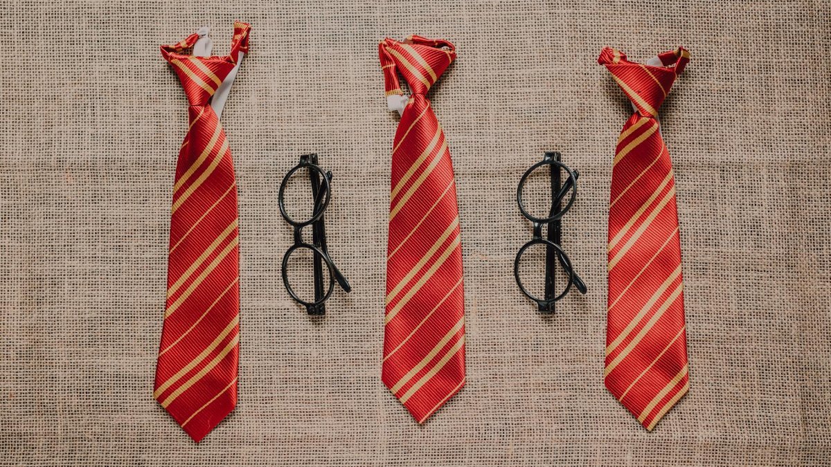 Three striped red ties and black eyeglasses on a textured burlap surface, evoking a wizard theme.