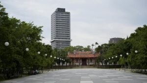 A towering skyscraper stands behind a historic pagoda amid trees in an urban park.