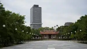 A towering skyscraper stands behind a historic pagoda amid trees in an urban park.