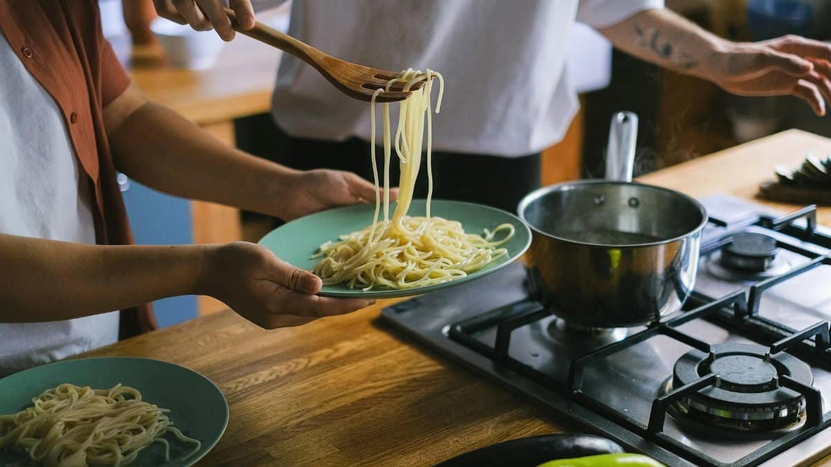 Two people preparing spaghetti in a cozy kitchen setting.