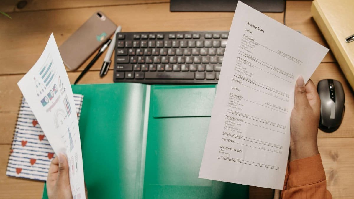 Hands holding and reviewing balance sheets over a desk with a keyboard and stationery.