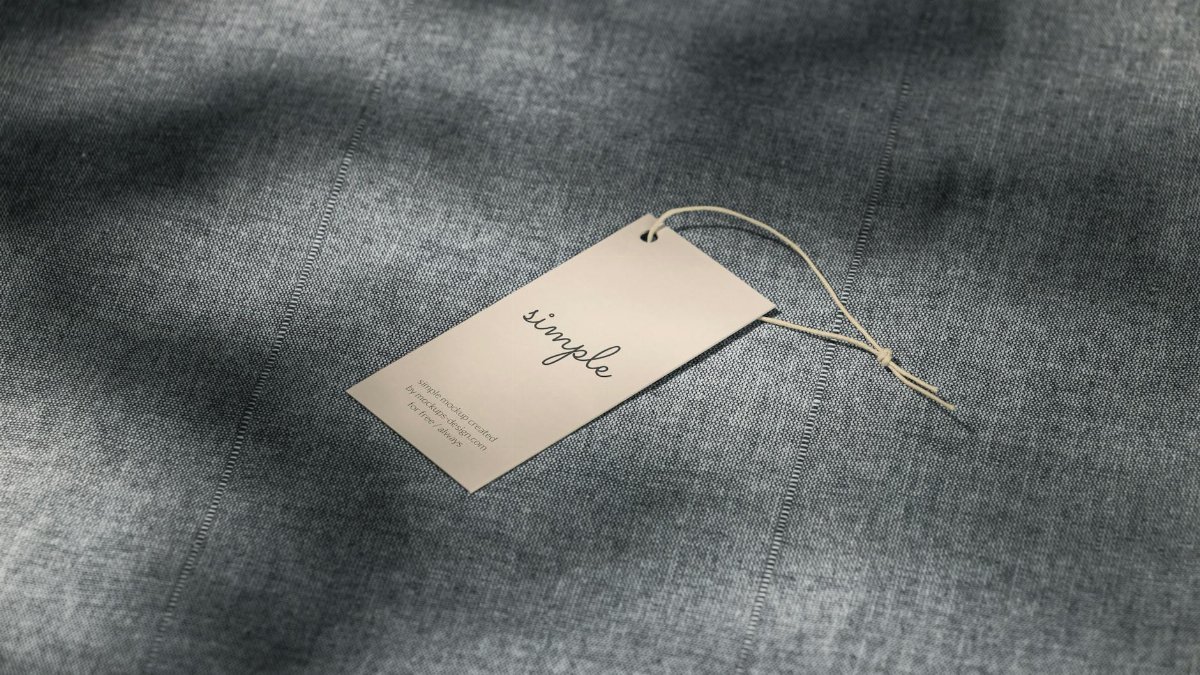 A simple clothing tag resting on a textured gray fabric surface with soft lighting.
