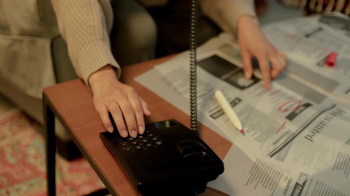 Woman using a landline and newspaper for a job search, highlighting domestic life.