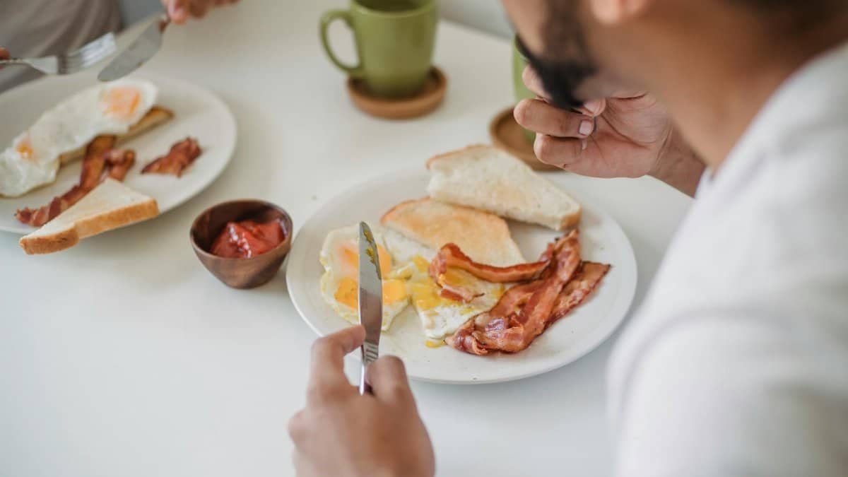 A casual breakfast scene with bacon, eggs, toast, and coffee shared by two people.