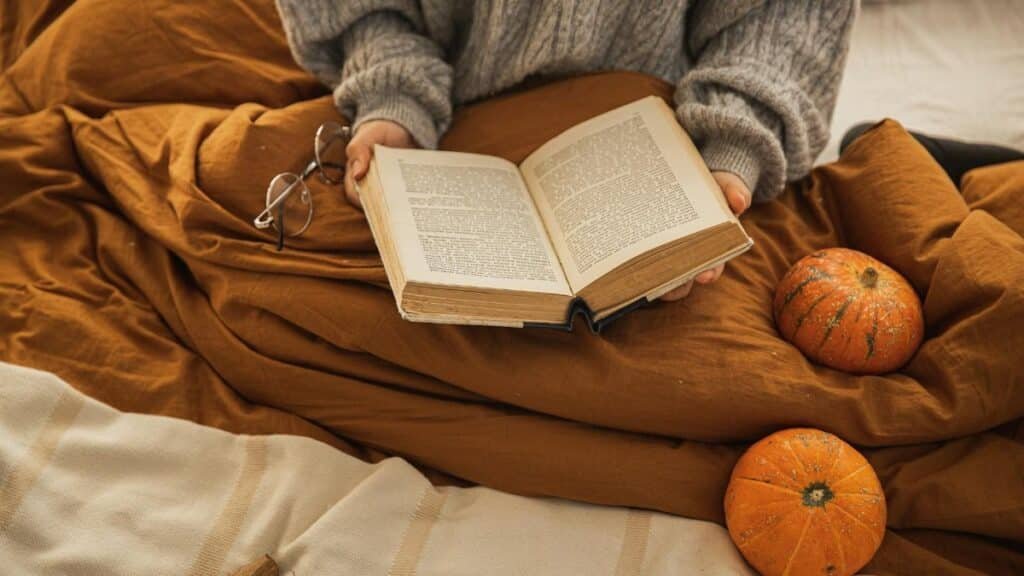 A person reading a book in a cozy setting with pumpkins, embodying autumn relaxation.
