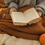 A person reading a book in a cozy setting with pumpkins, embodying autumn relaxation.