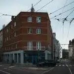 A red brick building at a quiet urban street intersection with overhead cables.