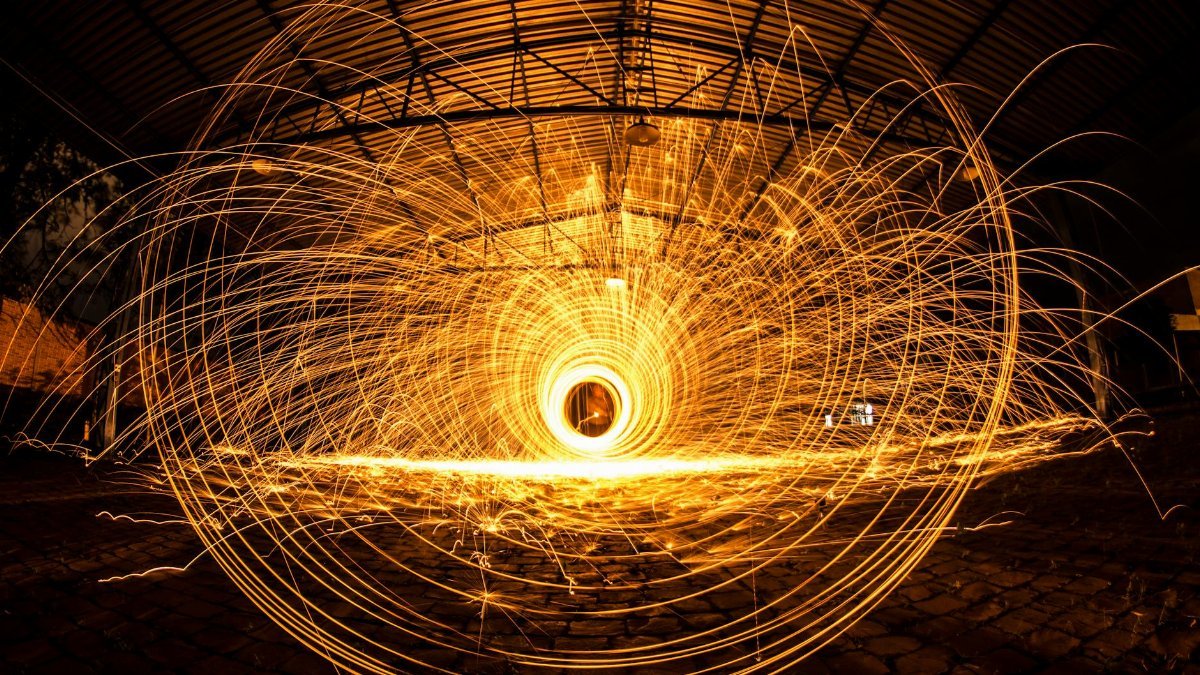 Mesmerizing long exposure of vibrant steel wool sparks creating circular patterns indoors.