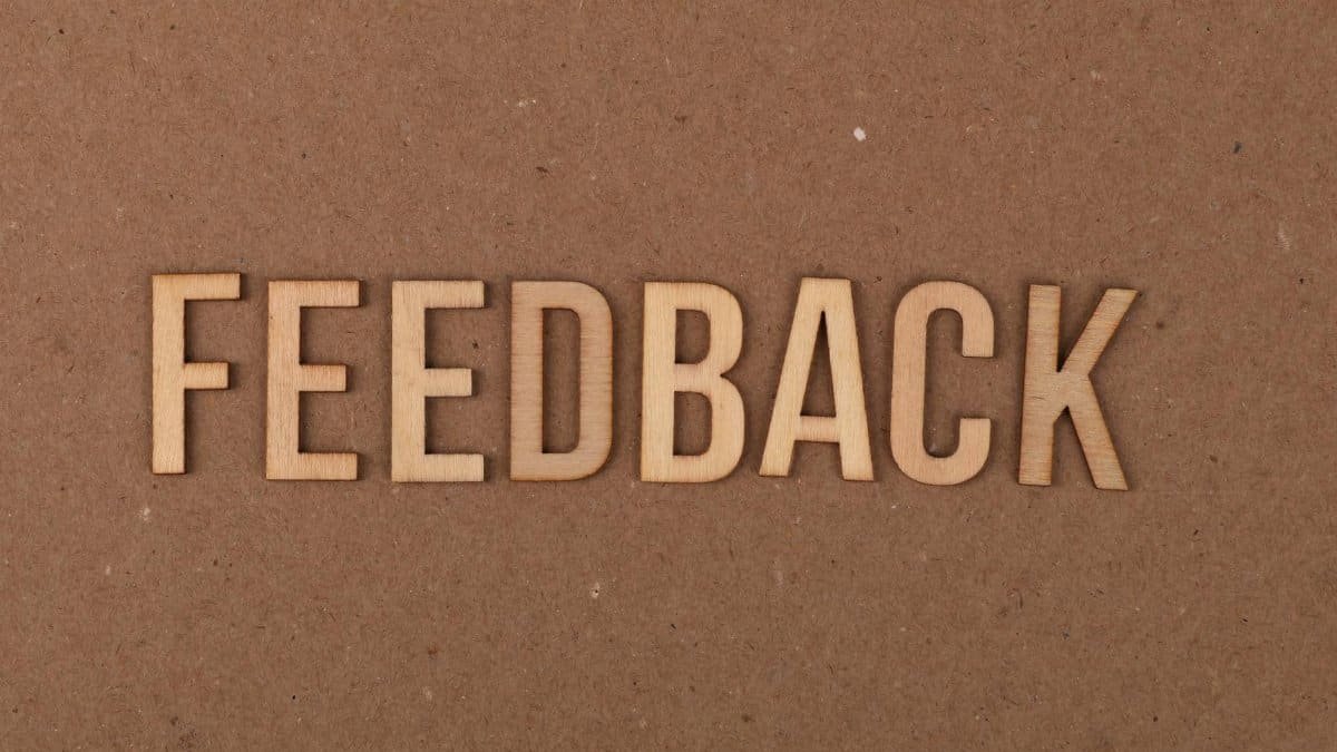 A close-up of a wooden 'FEEDBACK' sign on a textured cardboard background.