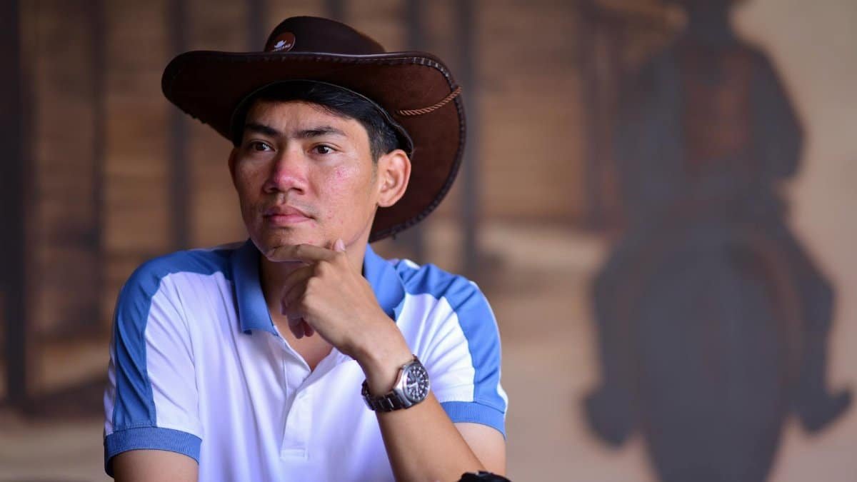 Thoughtful man in cowboy hat with Western mural background. Casual attire and contemplative pose.