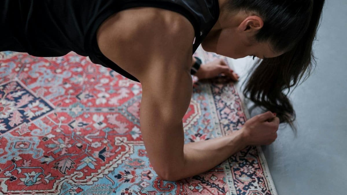 Woman performing a plank exercise on a patterned rug, showcasing muscular strength and focus.
