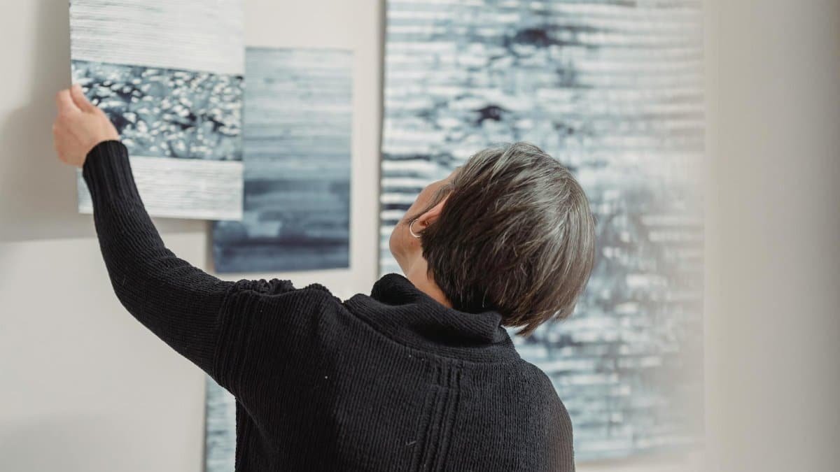 A woman arranges abstract art pieces on a gallery wall, showcasing modern creativity.