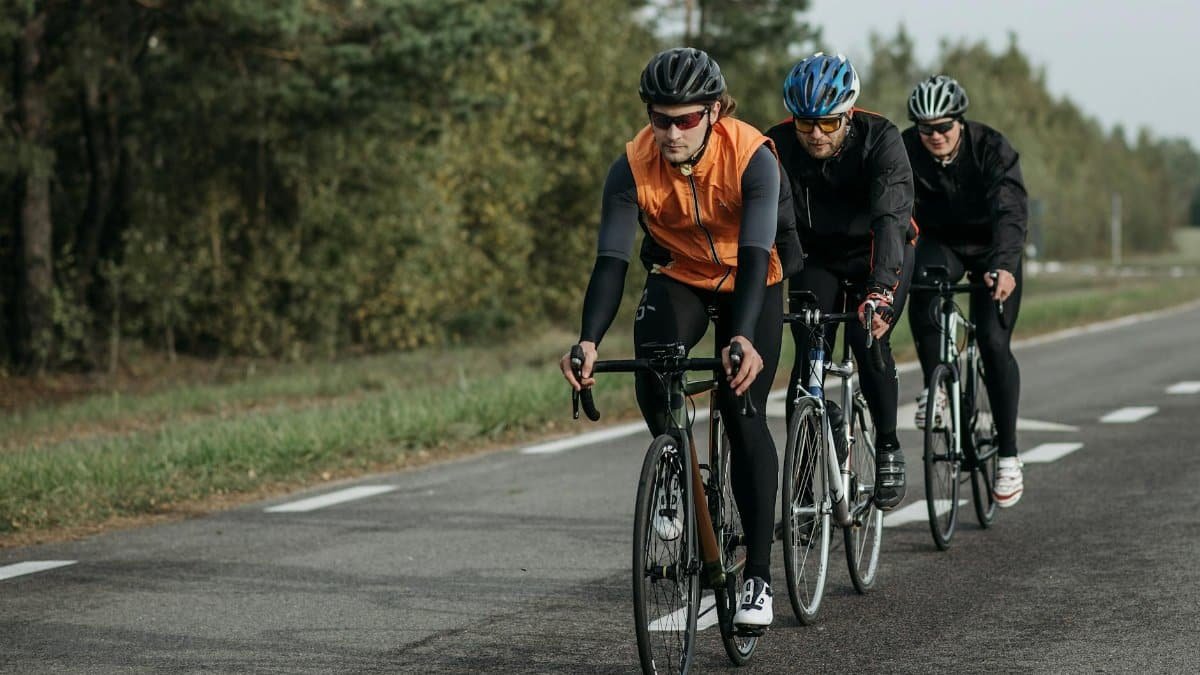 Three cyclists in gear ride along a tree-lined road, showcasing endurance and teamwork in outdoor cycling.