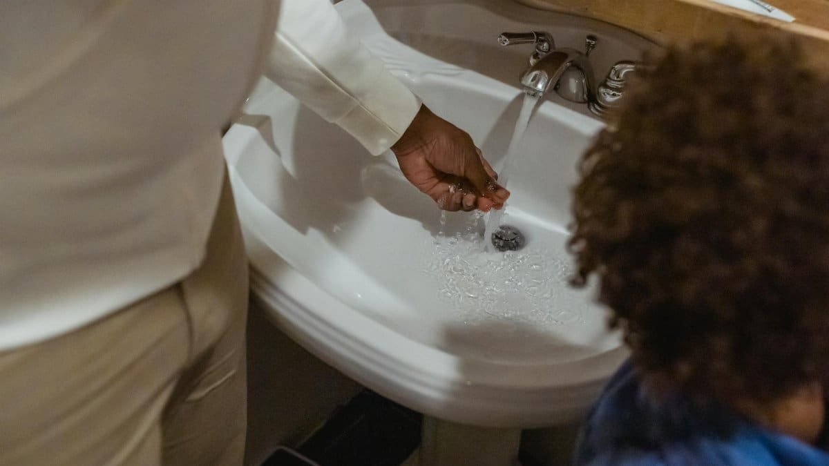 A parent and child share a daily hand-washing routine at the bathroom sink, emphasizing hygiene and bonding.