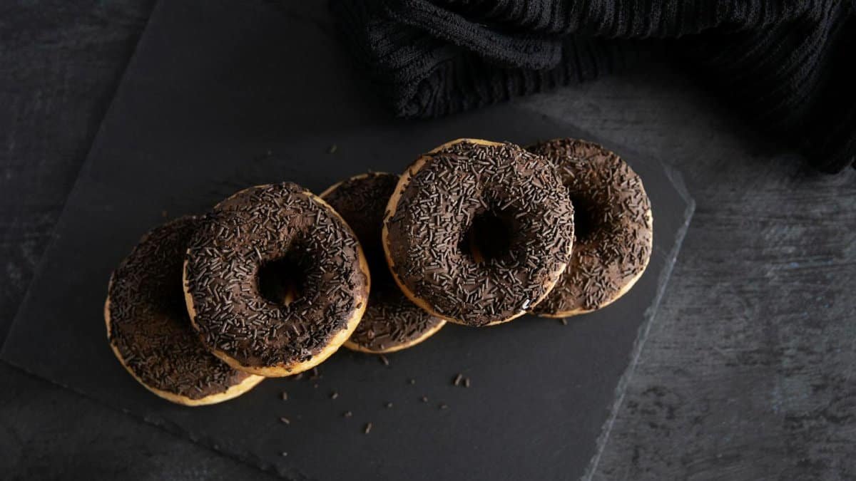 A tempting display of chocolate doughnuts with sprinkles on a dark slate background, perfect for dessert lovers.