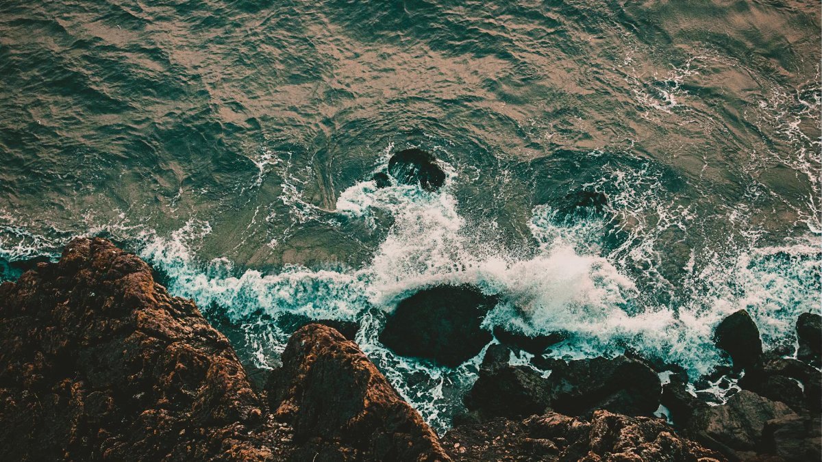 A breathtaking aerial shot of waves crashing on a rocky shoreline, showcasing nature's raw beauty.