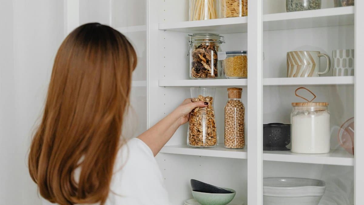 Woman arranging jars on pantry shelves for organized food storage.