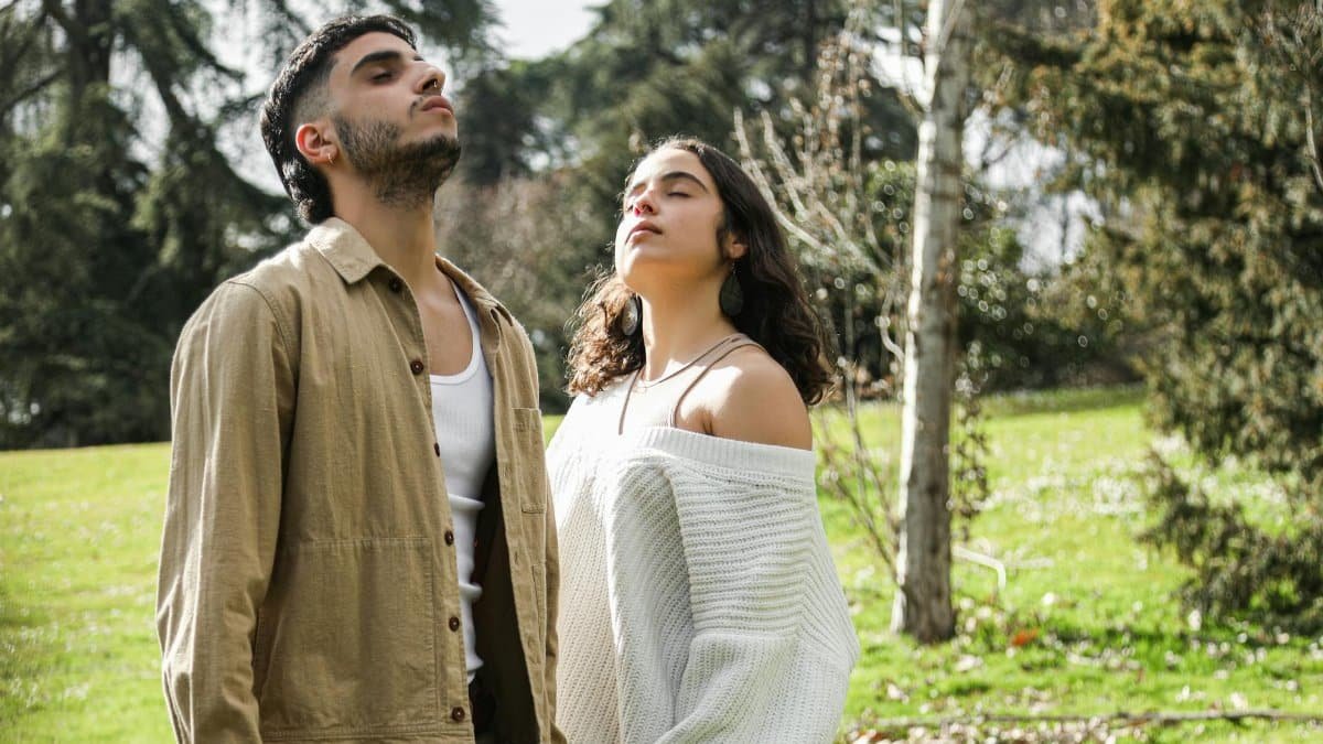 A man and woman enjoy deep breathing exercises outdoors in a lush green park.