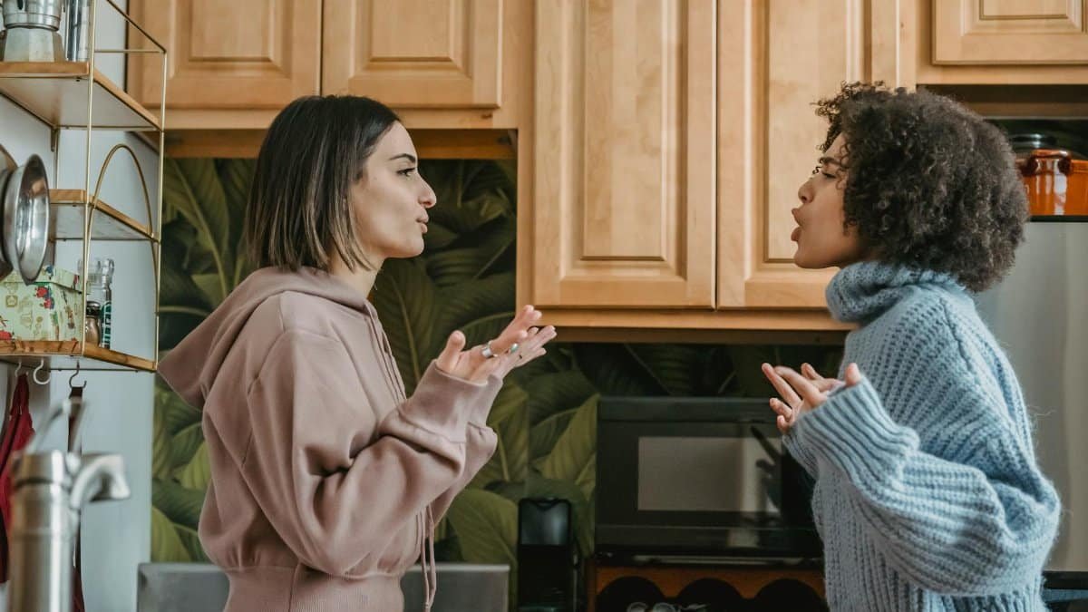 A heated discussion between two young women in a contemporary kitchen setting.