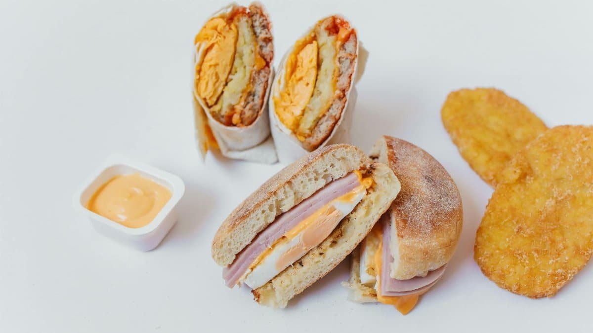 A mouth-watering breakfast spread featuring a sandwich, wrap, and hash browns on a white surface.