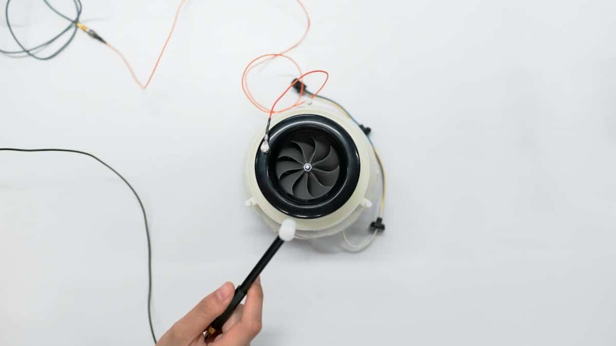 Overhead view of a hand adjusting a small electric fan with wires on a white surface.