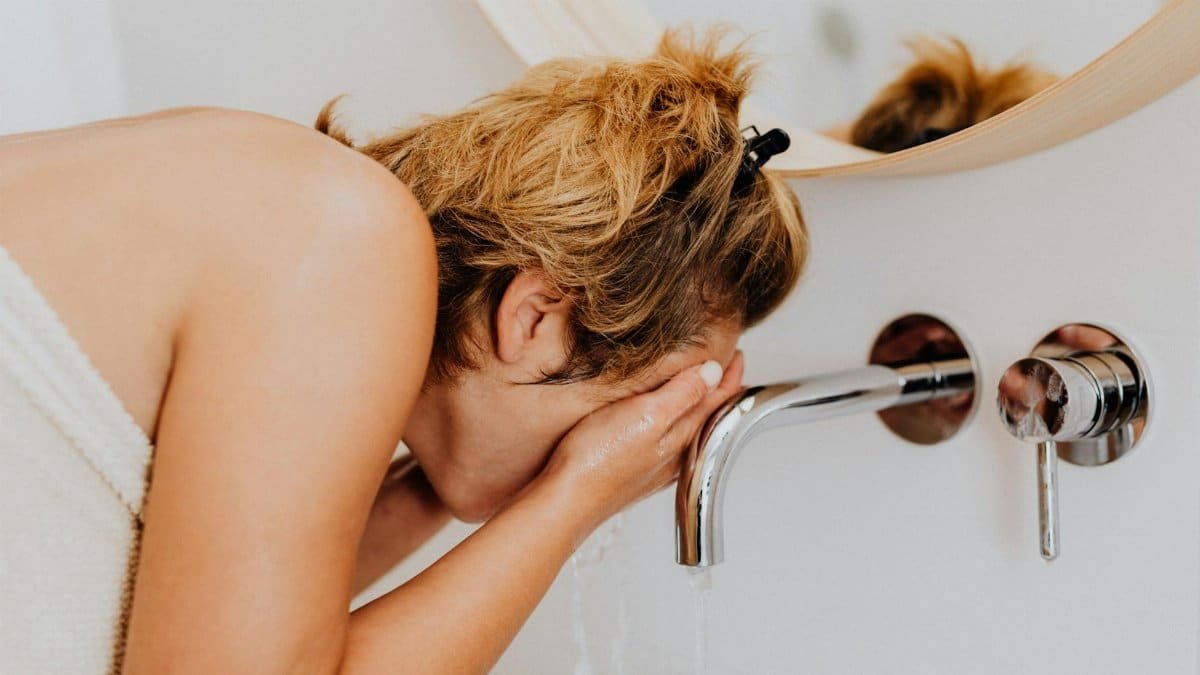 Adult woman washing her face at a modern bathroom sink during the morning routine.