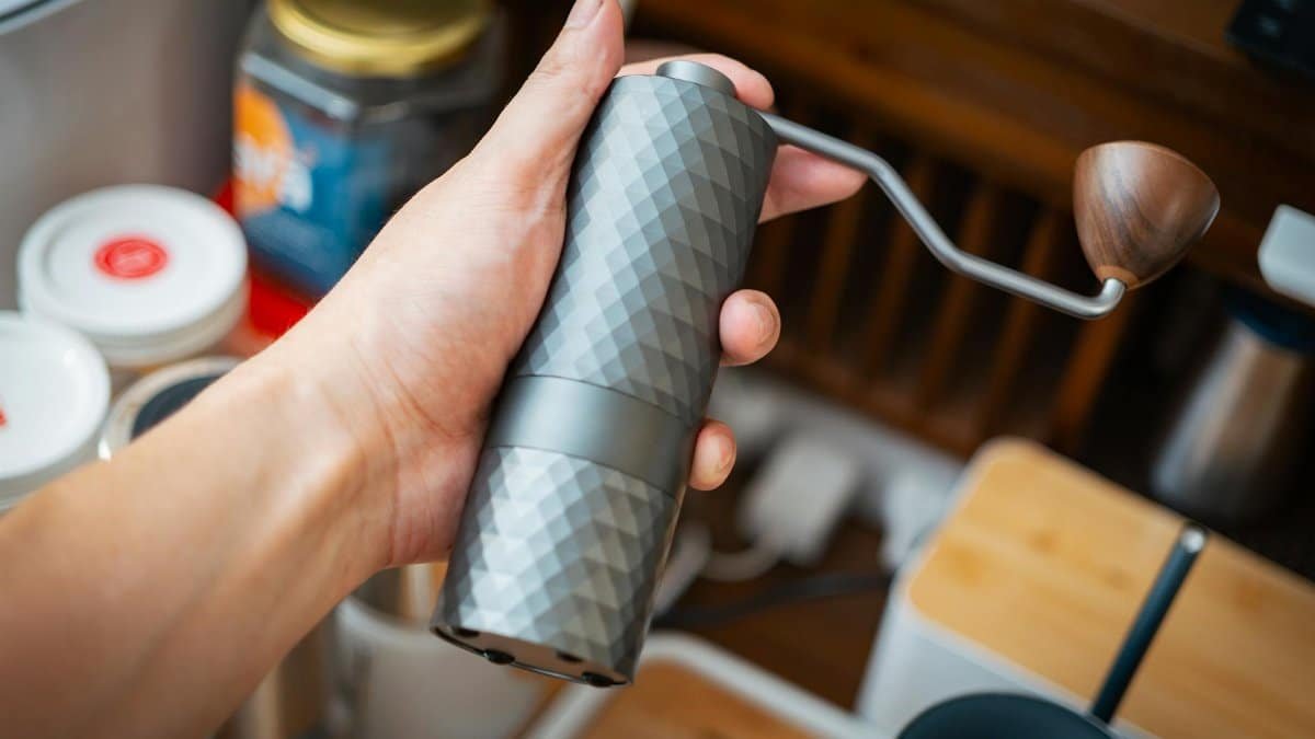 A close-up of a hand holding a stylish coffee grinder in a cozy kitchen environment.