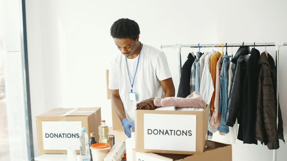 A volunteer organizes donations in a community center, featuring boxes labeled "Donations" and a clothing rack.