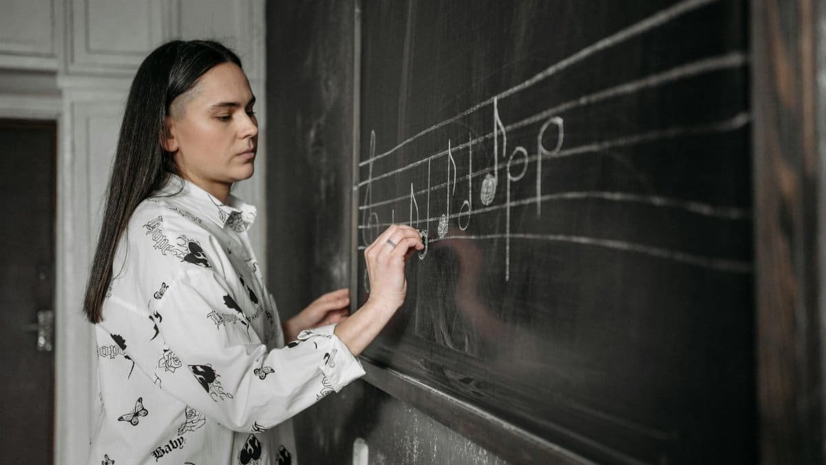 A woman drawing musical notes on a chalkboard in a classroom setting.