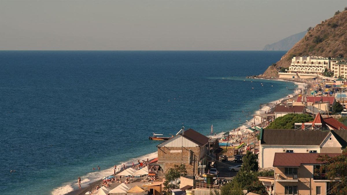 View of a coastal town with beachgoers, buildings, and the sea stretching into the horizon.