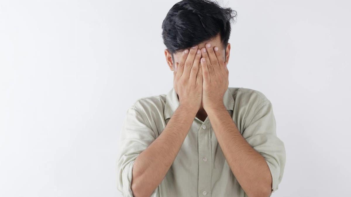 A man covering his face with hands, expressing feelings of stress and emotional struggle.