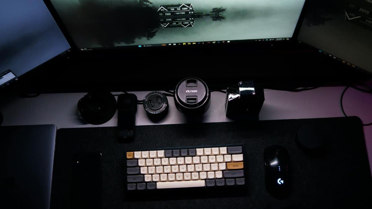 Minimalist work from home setup with triple monitors, keyboard, and tech accessories.