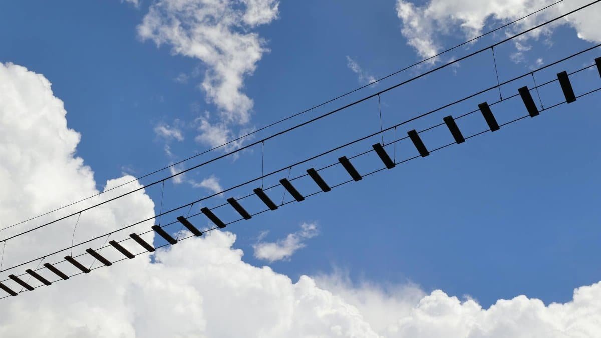 A low angle view of a suspended footbridge set against a vibrant blue sky and clouds.