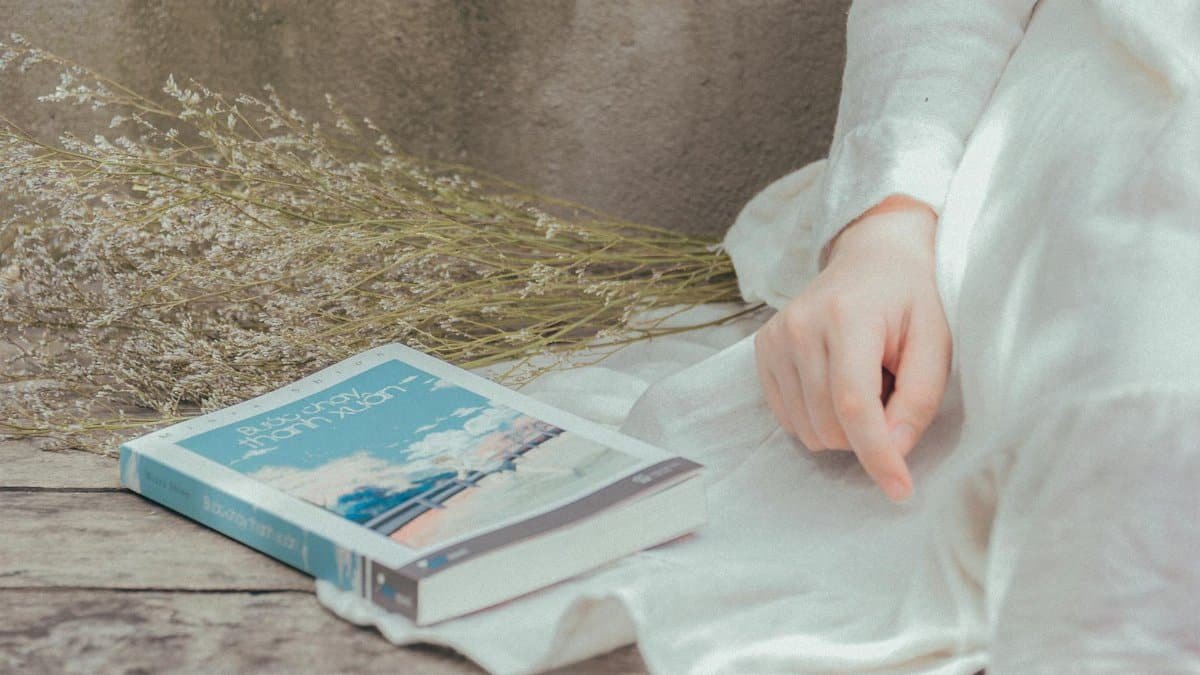 A peaceful moment outdoors with a book, dry flowers, and relaxing white attire.
