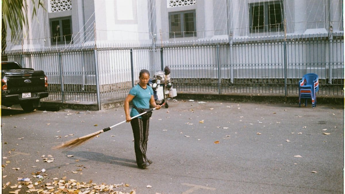 A woman sweeping leaves on a street in Ho Chi Minh City, showcasing daily urban life.