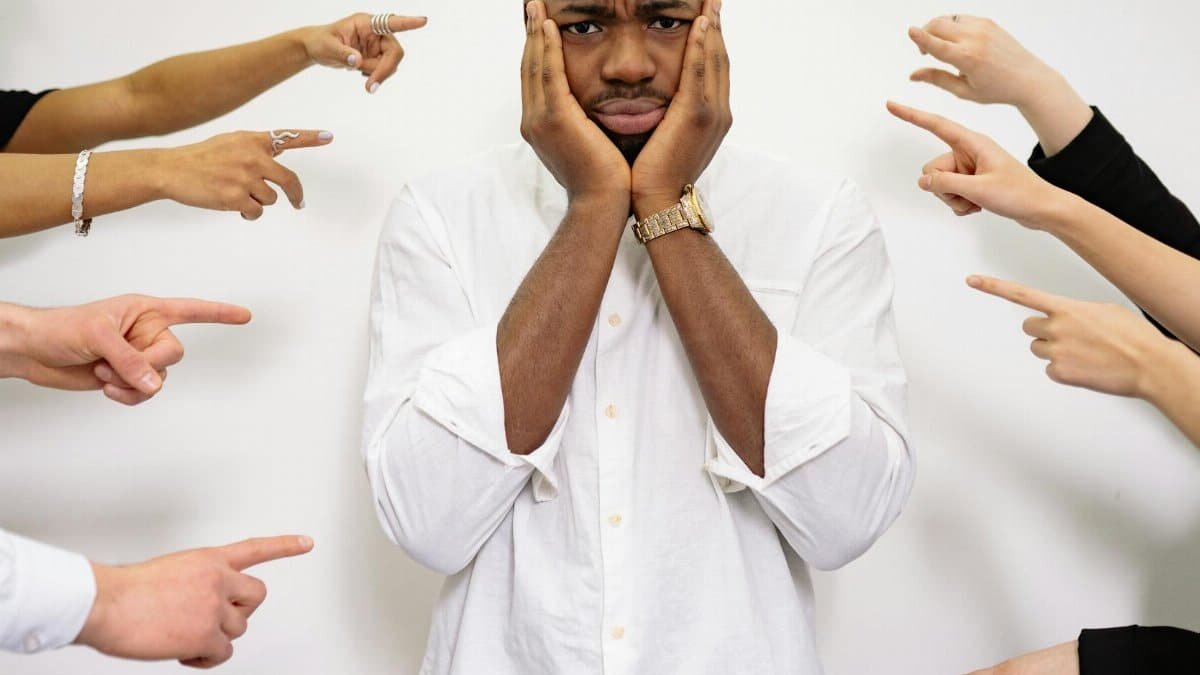 Worried man surrounded by pointing fingers, symbolizing bullying and social pressure.